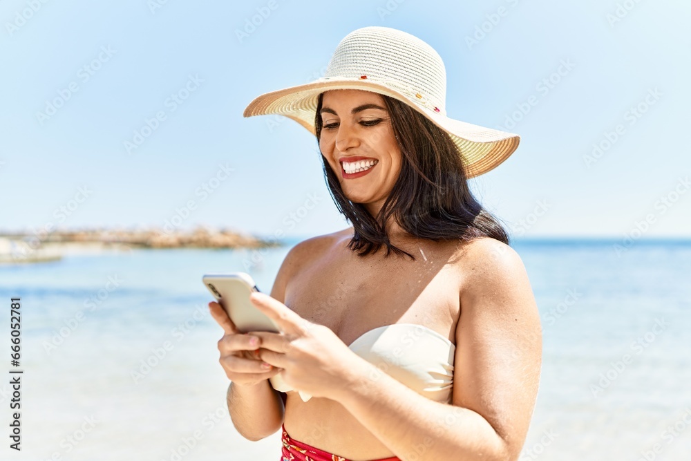 Young beautiful hispanic woman tourist smiling confident using smartphone at seaside