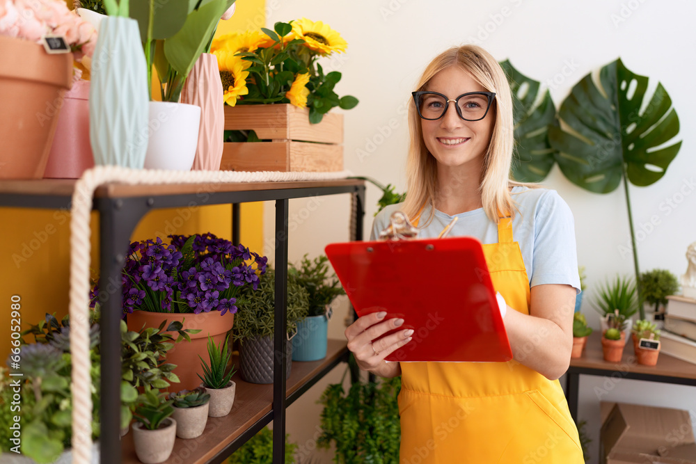 Young blonde woman florist smiling confident writing on document at flower shop