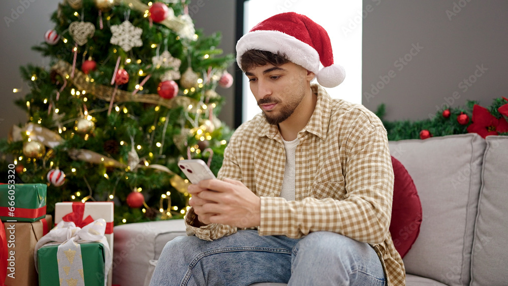 Young arab man using smartphone sitting by christmas tree at home Young arab man using smartphone sitting by christmas tree at home