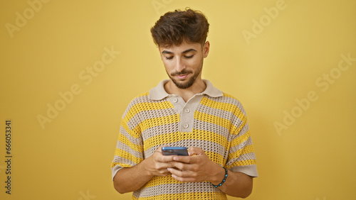Cool arabian dude, a young adult, fully immersed, fired up in sending out a serious message on his smartphone. masterstroke in tech chutzpah, concentrates facing the isolated yellow backdrop. photo