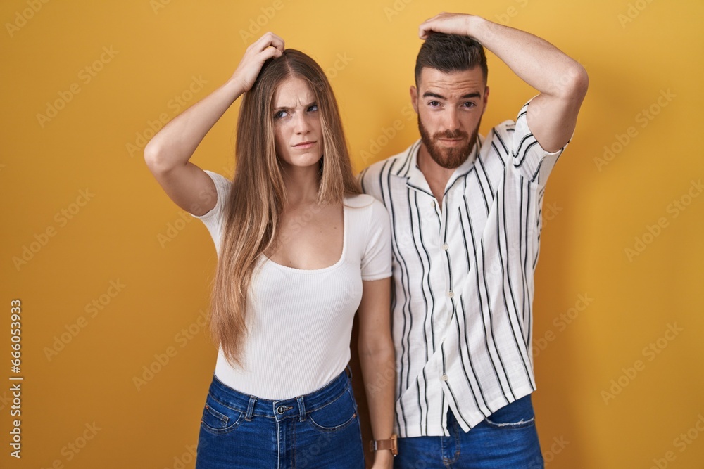 Young couple standing over yellow background confuse and wondering about question. uncertain with doubt, thinking with hand on head. pensive concept. Young couple standing over yellow background confuse and wondering about question. uncertain with doubt, thinking with hand on head. pensive concept.