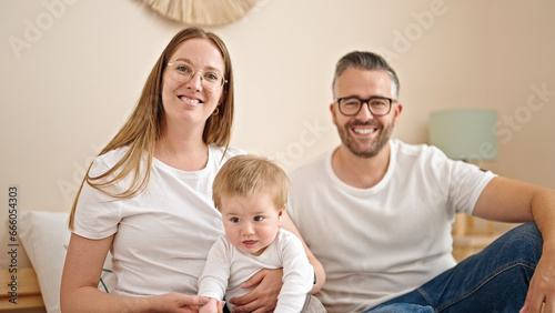 Family of mother, father and baby smiling together looking a the camera at bedroom