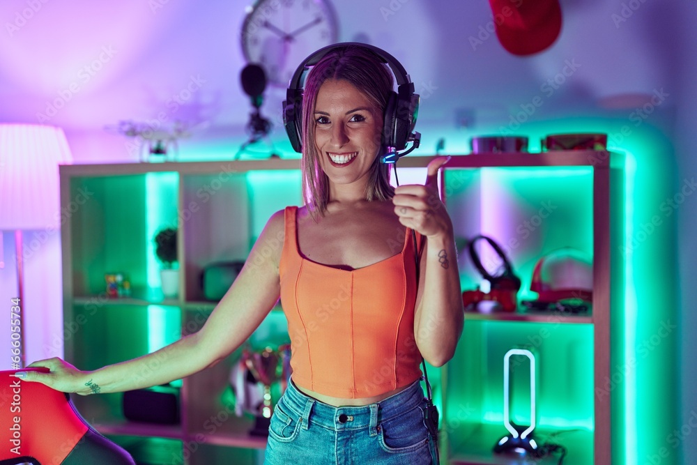 Young woman playing video games wearing headphones smiling happy and positive, thumb up doing excellent and approval sign Young woman playing video games wearing headphones smiling happy and positive, thumb up doing excellent and approval sign