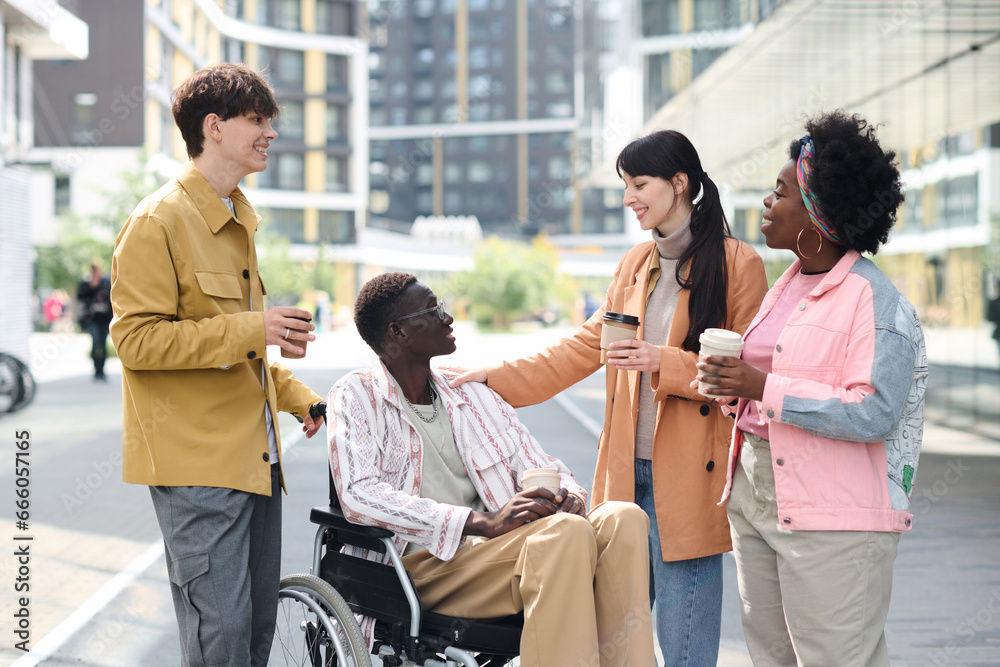 Group of young friends spending time together outdoors, they drinking coffee and talking to their friend with disability Group of young friends spending time together outdoors, they drinking coffee and talking to their friend with disability