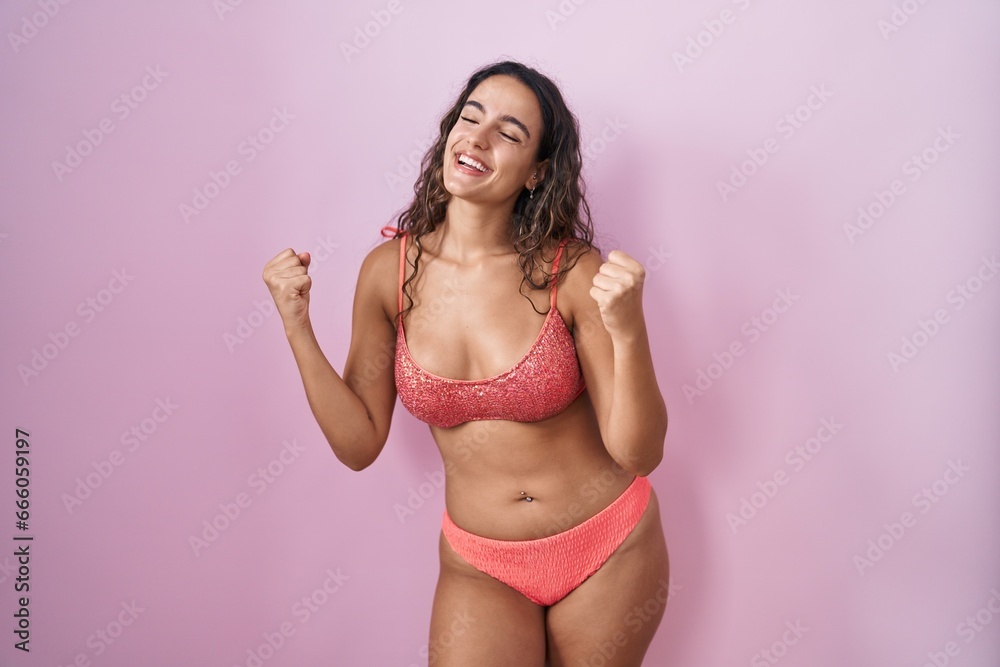 Obraz premium Young hispanic woman wearing lingerie over pink background very happy and excited doing winner gesture with arms raised, smiling and screaming for success. celebration concept.
