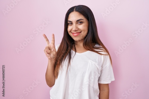 Young arab woman standing over pink background showing and pointing up with fingers number two while smiling confident and happy.