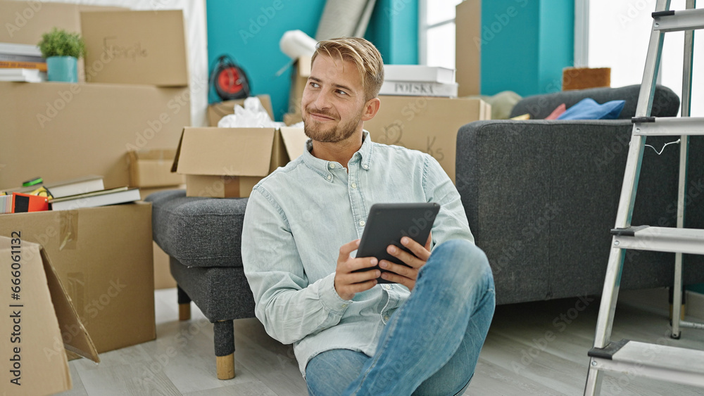 Young caucasian man using touchpad sitting on floor at new home Young caucasian man using touchpad sitting on floor at new home