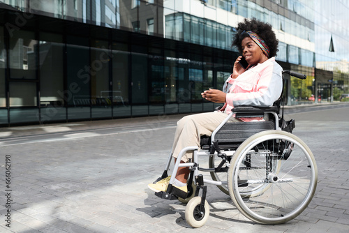 African American woman with disability talking on mobile phone while sitting in wheelchair in the city