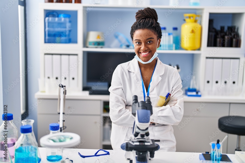 African american woman scientist wearing medical mask with arms crossed gesture at laboratory