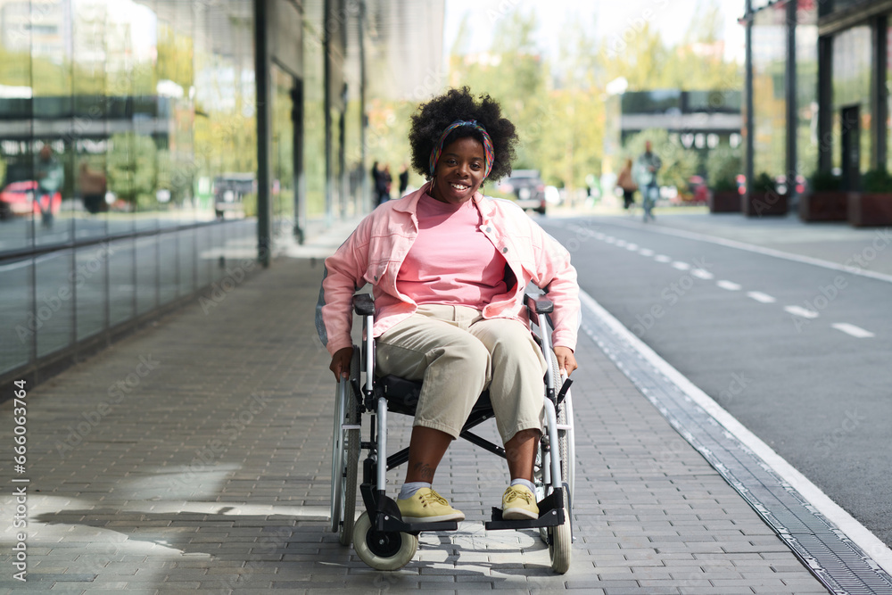 Portrait of African American woman with disability smiling at camera while sitting in wheelchair in the city