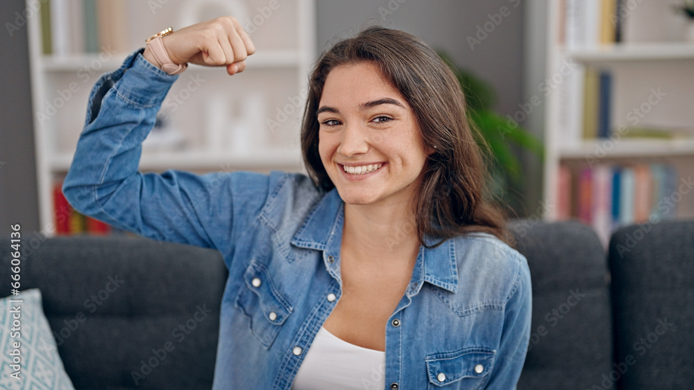 Young beautiful hispanic woman sitting on sofa doing power gesture with arm at home