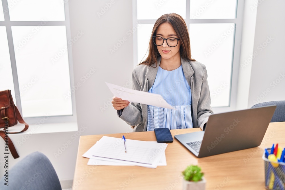 Young beautiful hispanic woman business worker using laptop reading document at office Young beautiful hispanic woman business worker using laptop reading document at office