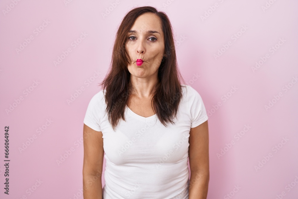 Middle age brunette woman standing over pink background making fish face with lips, crazy and comical gesture. funny expression.