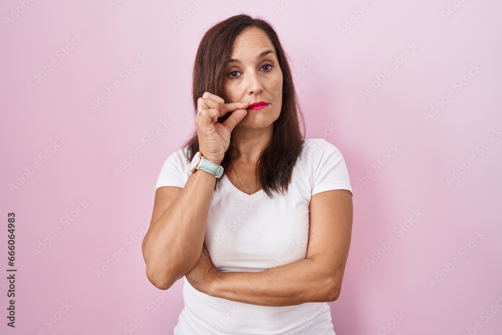 Middle age brunette woman standing over pink background mouth and lips shut as zip with fingers. secret and silent, taboo talking Middle age brunette woman standing over pink background mouth and lips shut as zip with fingers. secret and silent, taboo talking