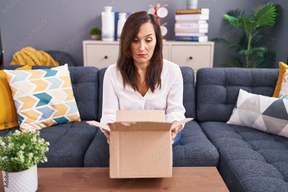 Middle age brunette woman opening cardboard box skeptic and nervous, frowning upset because of problem. negative person. Middle age brunette woman opening cardboard box skeptic and nervous, frowning upset because of problem. negative person.