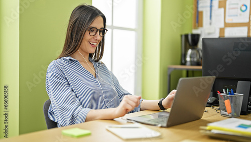 Young beautiful hispanic woman business worker using laptop and earphones smiling at office