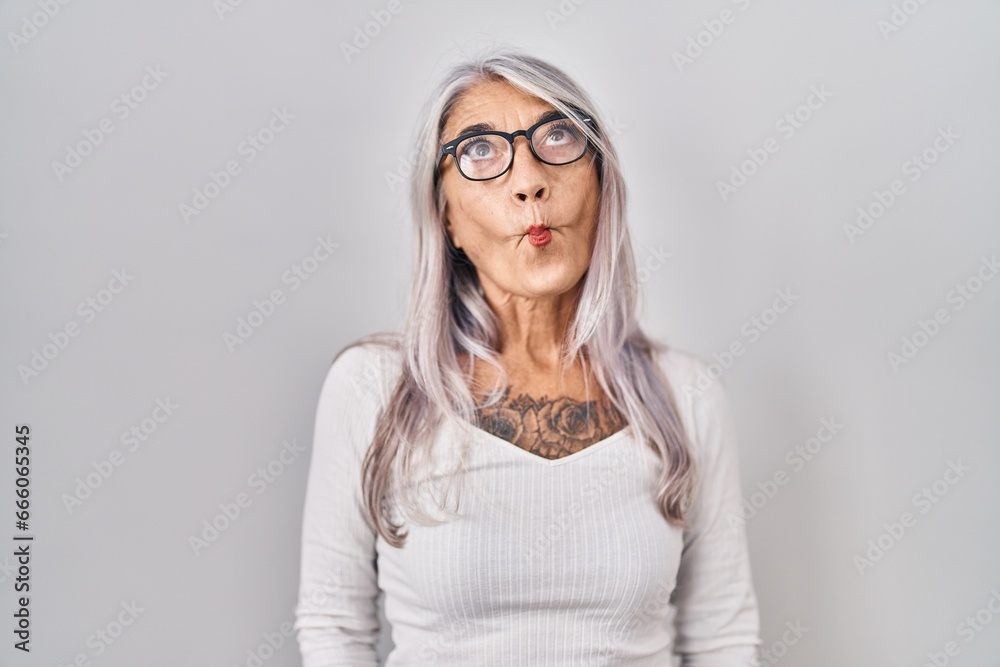 Middle age woman with grey hair standing over white background making fish face with lips, crazy and comical gesture. funny expression. - obrazy, fototapety, plakaty 