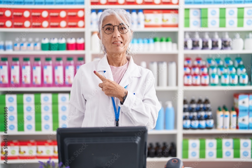 Middle age woman with tattoos working at pharmacy drugstore pointing aside worried and nervous with forefinger, concerned and surprised expression