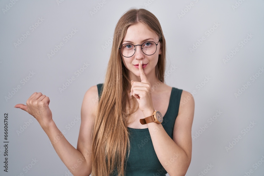 Φωτογραφία Young caucasian woman standing over white background asking to be quiet with finger on lips pointing with hand to the side