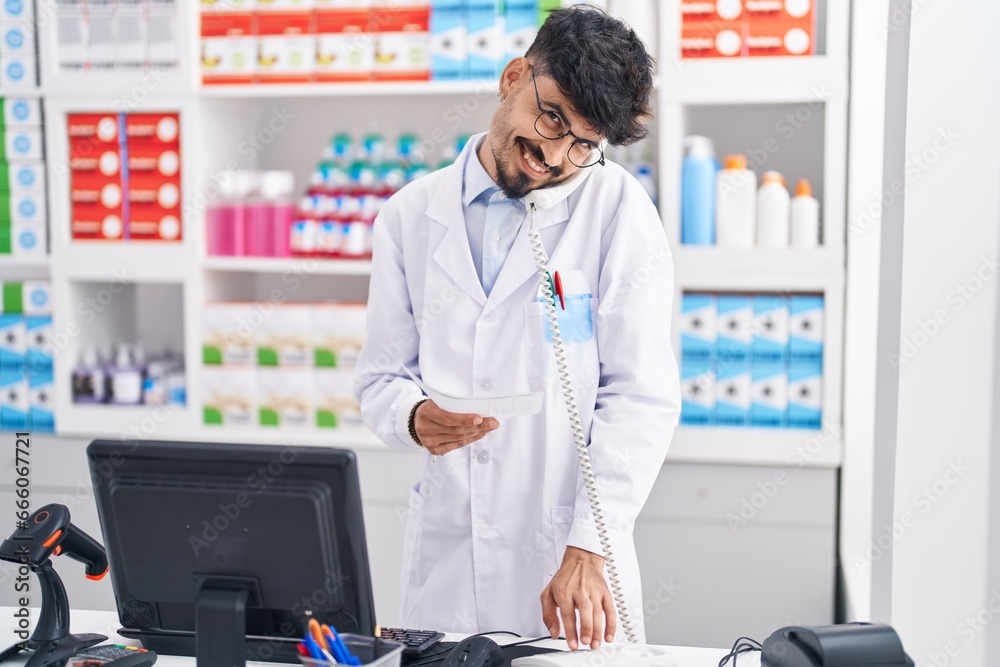 Young hispanic man pharmacist talking on telephone holding prescription at pharmacy Young hispanic man pharmacist talking on telephone holding prescription at pharmacy