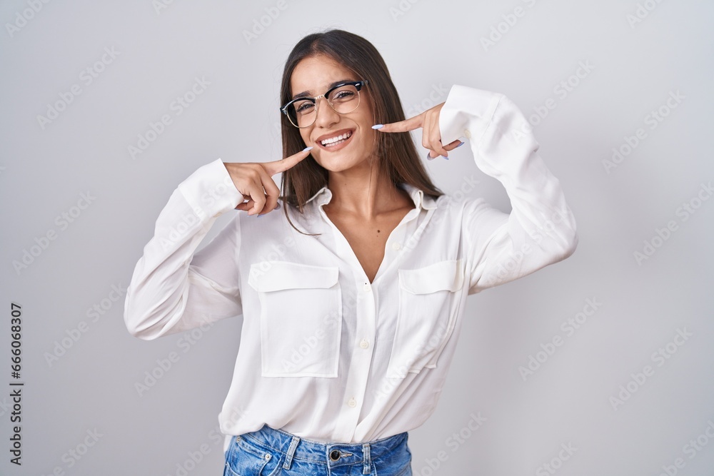 Young brunette woman wearing glasses smiling cheerful showing and pointing with fingers teeth and mouth. dental health concept. Young brunette woman wearing glasses smiling cheerful showing and pointing with fingers teeth and mouth. dental health concept.