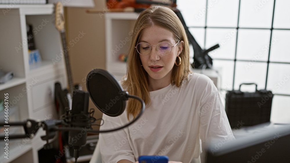 Young blonde woman radio reporter reading smartphone screen speaking on a show at radio studio Young blonde woman radio reporter reading smartphone screen speaking on a show at radio studio