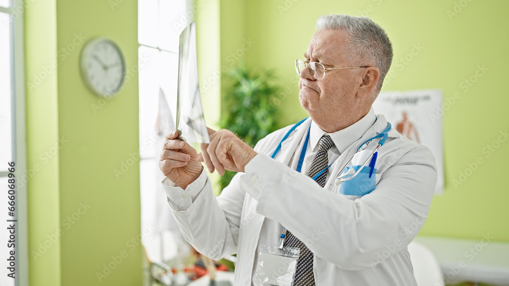 Fototapeta premium Middle age grey-haired man doctor looking xray at clinic