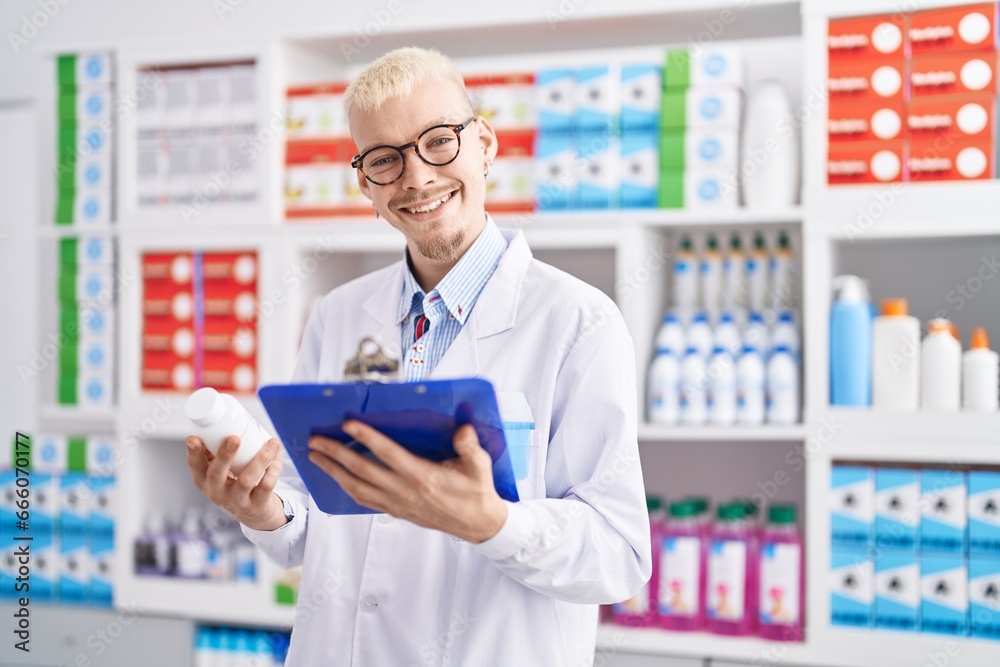 Young caucasian man pharmacist holding pills bottle reading report at pharmacy