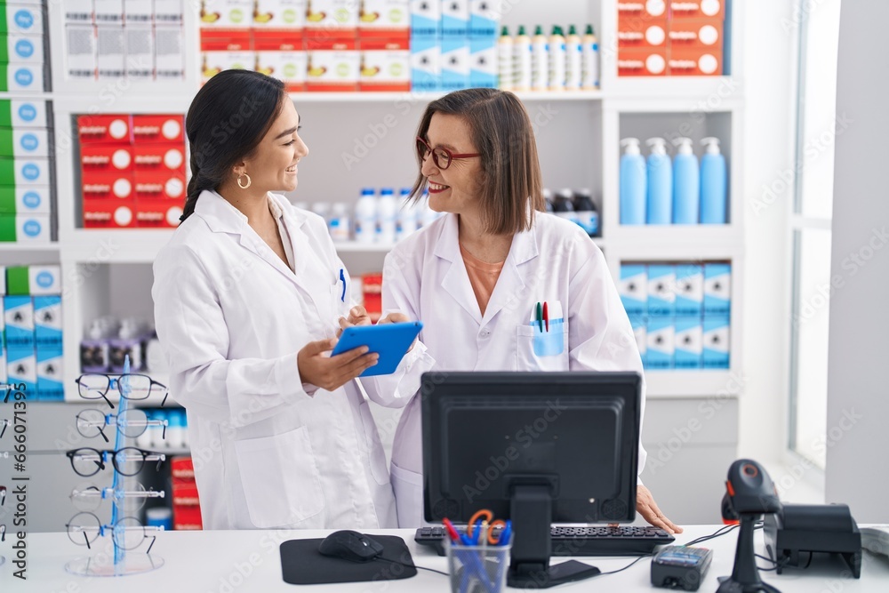 Two women pharmacist using computer and touchpad working at pharmacy