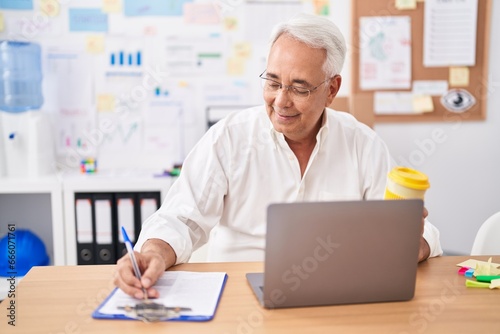 Middle age grey-haired man business worker using laptop writing on document at office