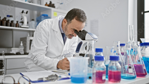 Aged man with grey hair  a scientist busy in his lab  peering into microscope for medical discovery