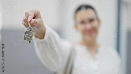 Young beautiful hispanic woman smiling holding new house keys at new house front door