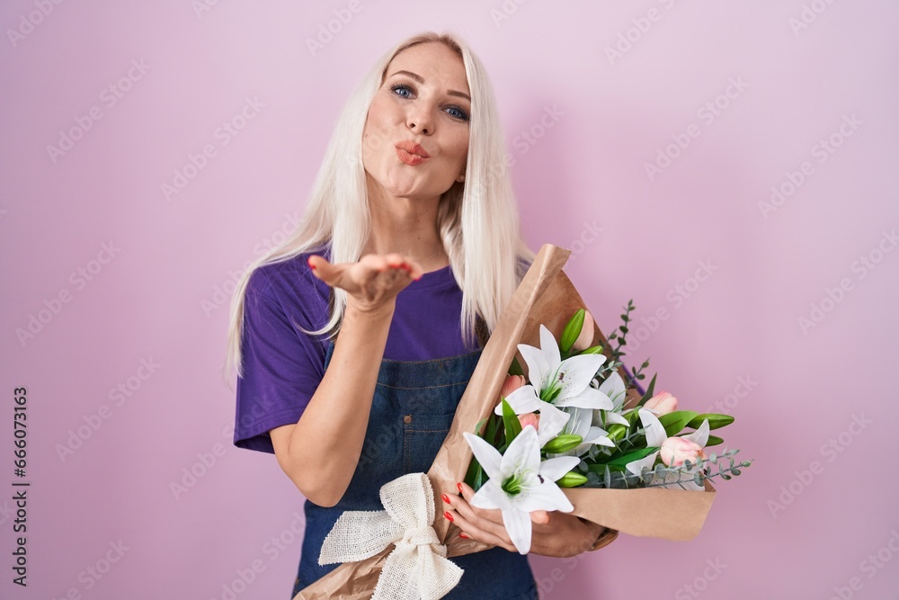 Caucasian woman holding bouquet of white flowers looking at the camera blowing a kiss with hand on air being lovely and sexy. love expression.
