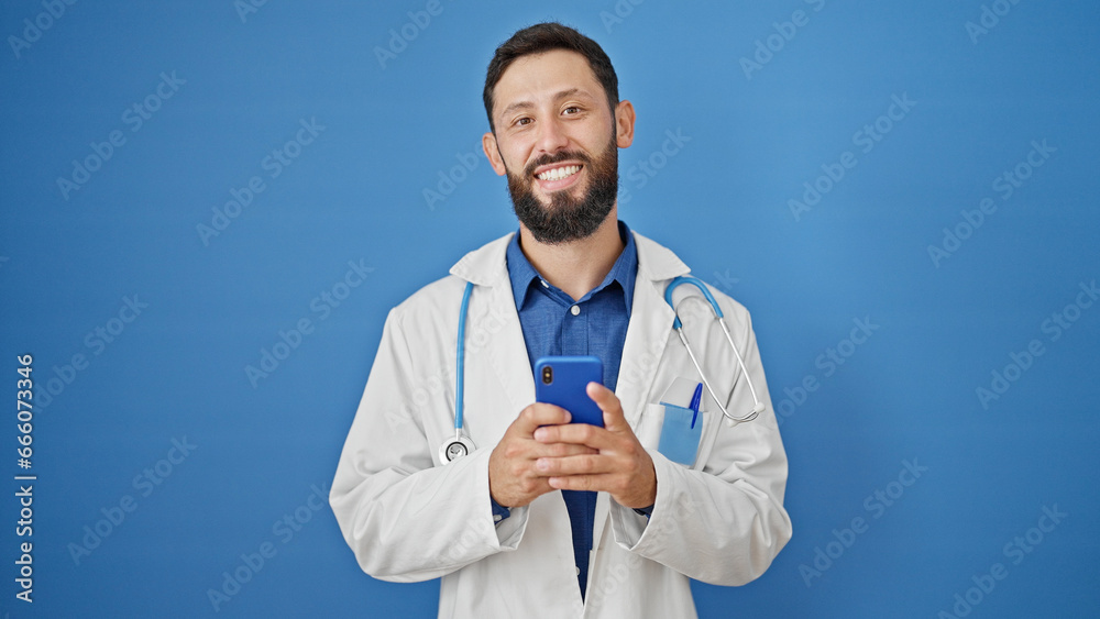 Young hispanic man doctor smiling using smartphone over isolated blue background Young hispanic man doctor smiling using smartphone over isolated blue background