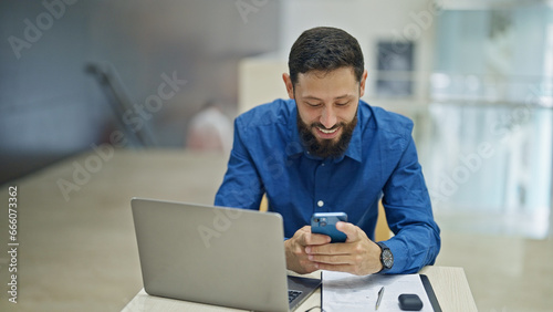 Young hispanic man business worker using laptop and smartphone at the office