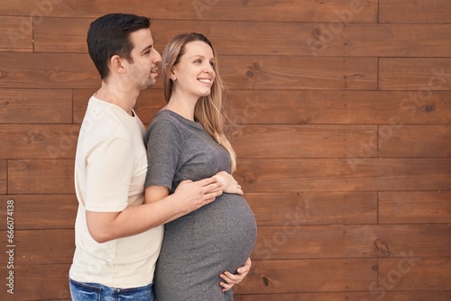 Man and woman couple hugging each other expecting baby over isolated wooden background