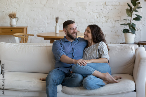Fotografie Joyful married couple relaxing on soft white home couch together, talking, chatt