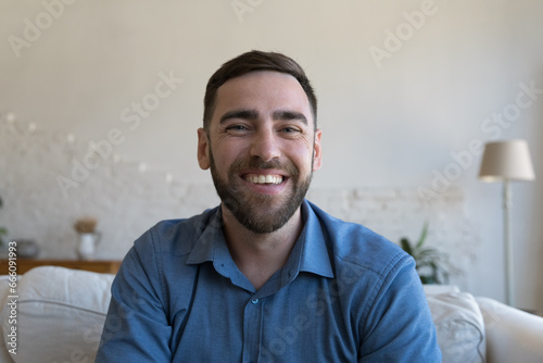 Cheerful handsome adult man home head shot portrait. Happy male model sitting on sofa, looking, speaking at camera, posing with toothy smile, laughing, speaking on video call, chat