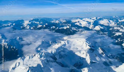 Aerial view of Alps mountain range with snow and blue sky.