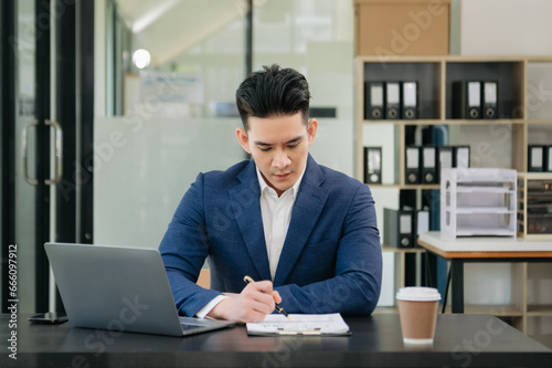 Confident Asian man with a smile standing holding notepad and tablet at the modern office.