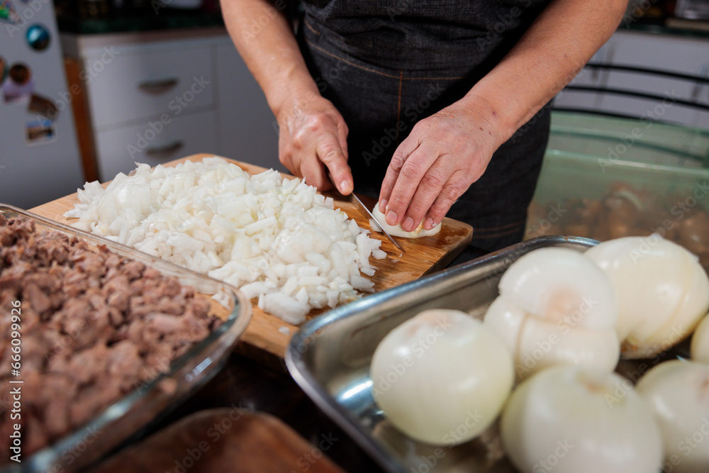 Close up of unrecognizable latin woman chopping onion and meat for filling chilean baked empanadas. Domestic kitchen