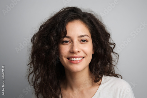 Everyday people. A smiling woman with long brown wavy hair. Pretty woman. On a grey background. Charming and graceful. Portrait.