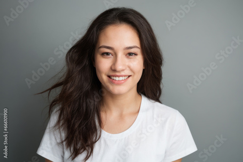 Everyday people. A smiling Australian woman. Brown eyes. Brown wavy hair over her shoulder. Wearing a white shirt. On a grey studio background. Portrait. Natural beauty. Natural glow. 