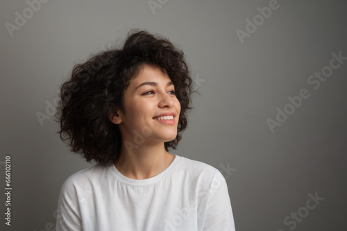 Everyday people. A smiling woman. Brown frizzy hair to her shoulders. Hair volume. Wearing a white shirt. On a light studio background. Portrait. Posing. Natural beauty. 