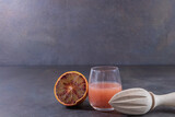 Jus fraîchement pressé d'orange sanguine dans un verre, avec une demi orange sanguine et un presse-agrume manuel en bois, sur fond uni avec espace négatif pour texte