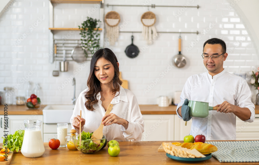 Young asian family couple having fun cooking and preparing cook vegan food healthy eat with fresh vegetable salad on counter in kitchen at home.Happy couple looking to preparing food