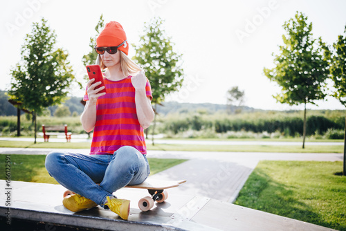 Young urban girl with her skateboard looking at smartphone outdoors. Happy young hipster woman with skateboard using mobile phone