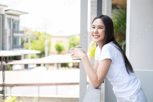 Young Asian beautiful woman drinking coffee and looking away with snile of happiness inthe moring, fresness moment for starting in morning. photo
