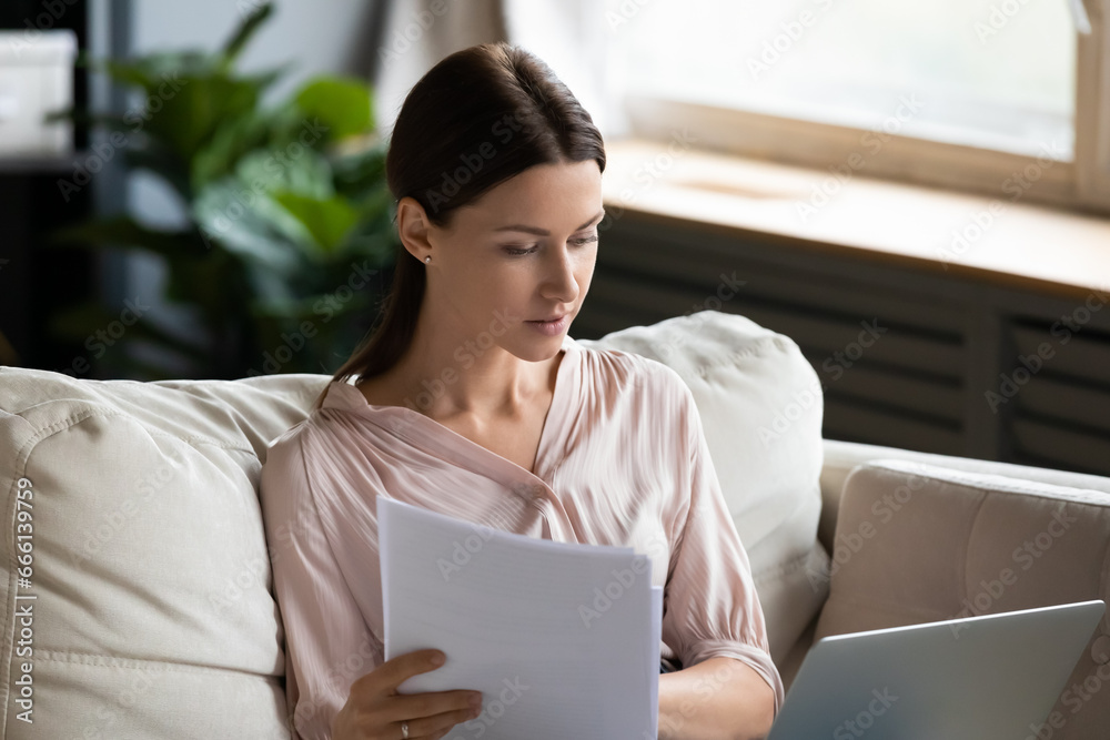 Workaholic woman on weekend do work at home sit on couch, self-employed female hold documents check data using pc looks at screen working, usage of e-banking, housewife and household utilities review Workaholic woman on weekend do work at home sit on couch, self-employed female hold documents check data using pc looks at screen working, usage of e-banking, housewife and household utilities review