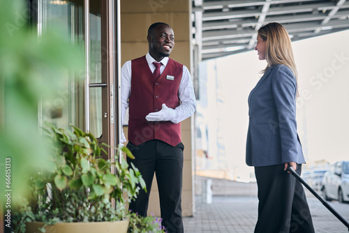 African American doorman greeting guest and opening door for her while she entering in the hotel